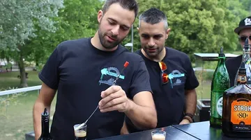 Two men mix drinks at an outdoor bar.