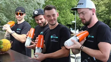 Four bartenders shake cocktails against a green backdrop.