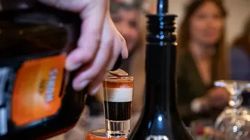 A hand pours a multi-layered cocktail into a glass.