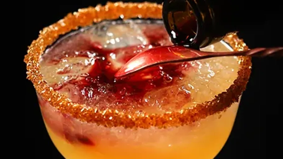 Glass with drink; syrup is poured in; dark background.