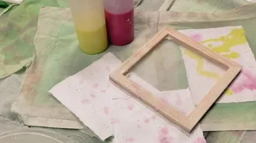 Two bottles of paint next to an empty picture frame.