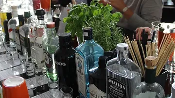 Bottle, ingredients are on a bar, guests mix cocktails.