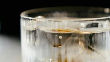 Glass with ice cubes and brown drink, dark background.