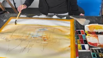 The artist paints with a brush on a large canvas.