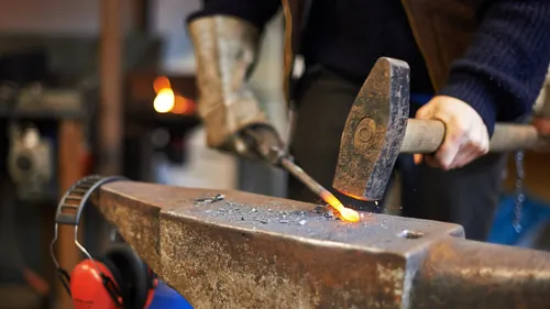 Schmied bearbeitet glühendes Metall auf Amboss in Werkstatt.