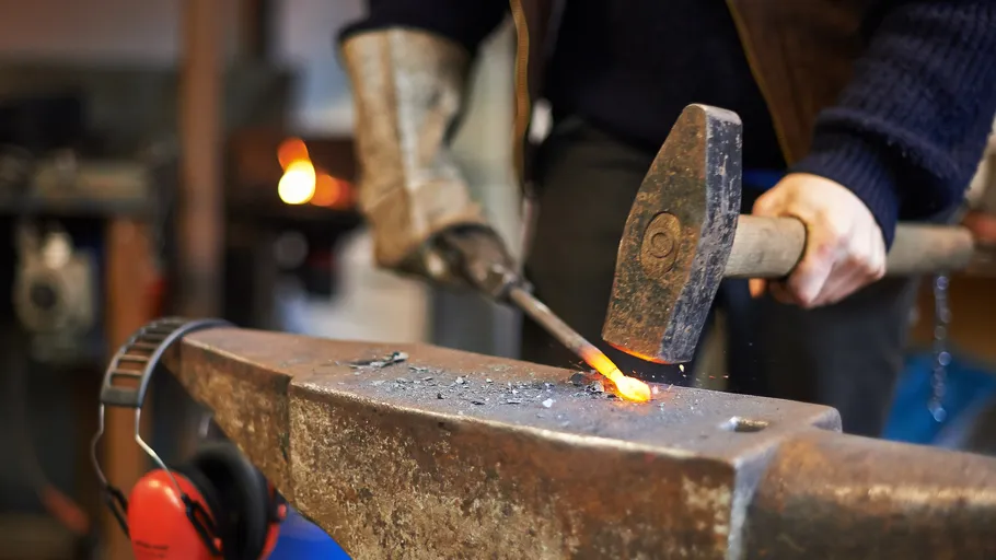 Schmied bearbeitet glühendes Metall auf Amboss in Werkstatt.