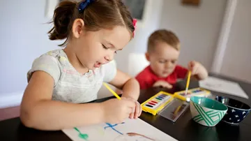Kinder malen mit Wasserfarben am Tisch im Innenbereich.