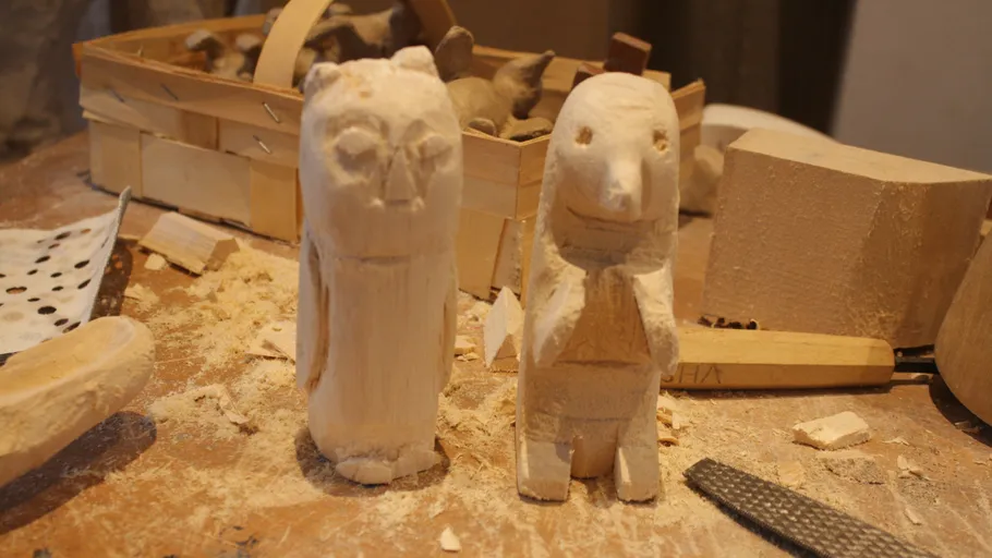 Two wooden sculptures on a messy workbench.