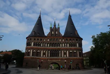 Historisches Gebäude mit Türmen, Menschen gehen vorbei.