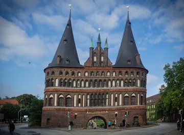 Stadt-Tor mit Türmen, Menschen passieren, umgebende Straße.