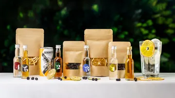 Bottle next to bags and a glass with a slice of lemon.