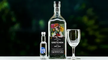 A bottle of gin is placed next to a glass on a table.