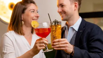 Two people toast with cocktails in a bar.