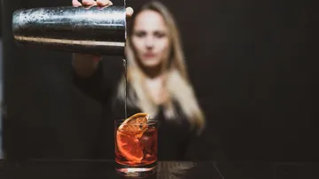 Shaker pours cocktail into glass with orange slice.