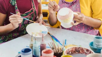 Two people paint crockery in a creative work space.