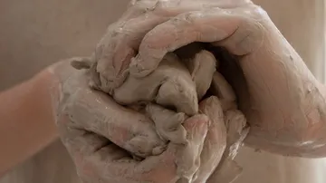 Hands knead moist clay in a creative environment.