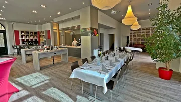 Restaurant mit gedeckten Tischen, Koch bereitet Speisen vor.