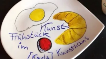 A plate with a drawn breakfast: egg, croissant, red dot.