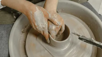 Hands form clay pot on turntable in workshop.