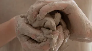 Hände formen feuchten Ton in einer kreativen Umgebung.