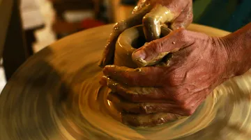 Hands form a clay cup on a potter's wheel.
