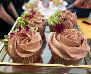 Cupcakes mit buntem Zuckerguss und essbaren Blumen auf Tablett.