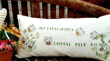 Kissen mit Bienenmotiven und der Aufschrift „Optimismus Summen mit Pollen“.