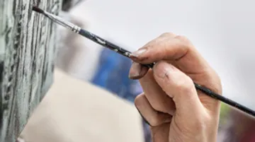 Hand holding brush, painting on a painted surface, studio