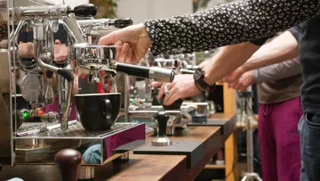 Barista operates machines while coffee flows into cups.