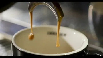 Drops of coffee fall into a black cup.