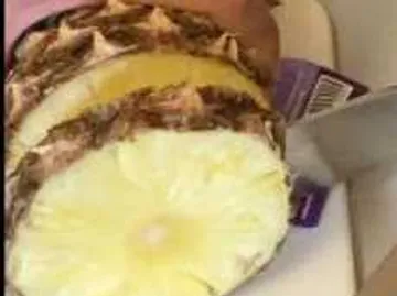Ananas wird mit einem Messer auf einem Schneidebrett geschnitten.