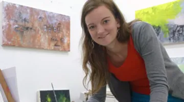 Frau steht an einem Tisch und malt in einem Atelier.