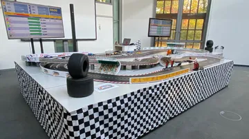 Slotcar-Rennbahn fährt unter Aufsicht von Bildschirmen.