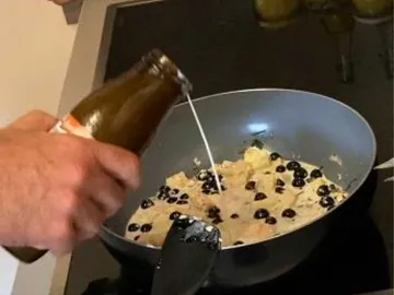 Eine Hand gießt Flüssigkeit in eine Pfanne mit Beeren.