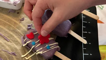 Purple cakelollies are decorated with colorful hearts and flowers.