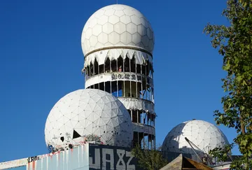 Grauer Turm mit gewölbten Fassaden, stark vandalisiert, im Freien.
