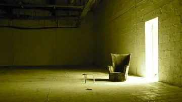 Ein Sessel steht neben einem kleinen Tisch in einem leeren Raum.