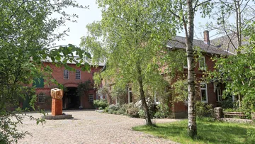 Red brick buildings surrounded by trees and sculpture.