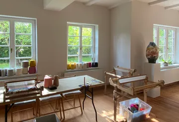 Helle Werkstatt mit Webrahmen, Garnen und Pflanzen draußen.
