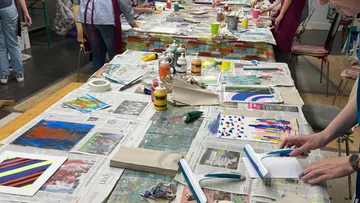 Tische mit Kunstmaterialien, Menschen gestalten kreative Arbeiten.
