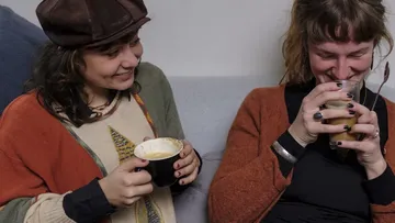 Zwei Frauen sitzen, lachen und trinken Kaffee.