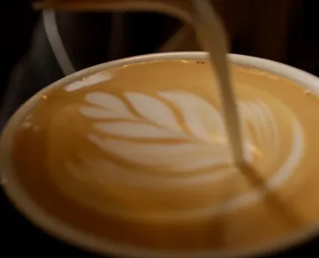 Coffee with an artistic milk foam pattern is poured.