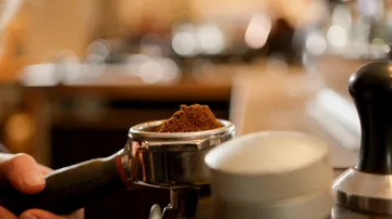 Kaffeepulver wird in einen Siebträger gedrückt, in einer Cafeteria.