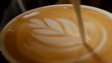 Milch wird in einen Kaffee gegossen, um ein Muster zu formen.