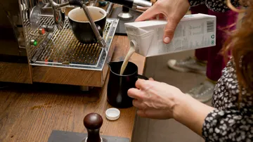 A person pours milk into a black jug.