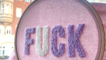 Embroidered word “FUCK” in a frame on pink fabric.