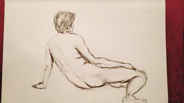 Naked person sits relaxed on the floor, sketching.