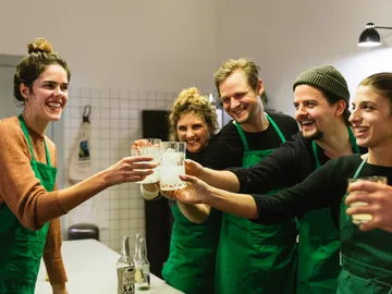 Sechsergruppe stößt mit Gläsern in einer modernen Küche an.