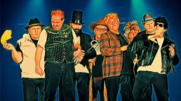 Acht Männer in auffälligen Outfits stehen dramatisch auf der Bühne.