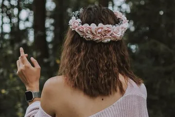 Frau mit Blumenkranz gestikuliert in einem Waldgebiet.
